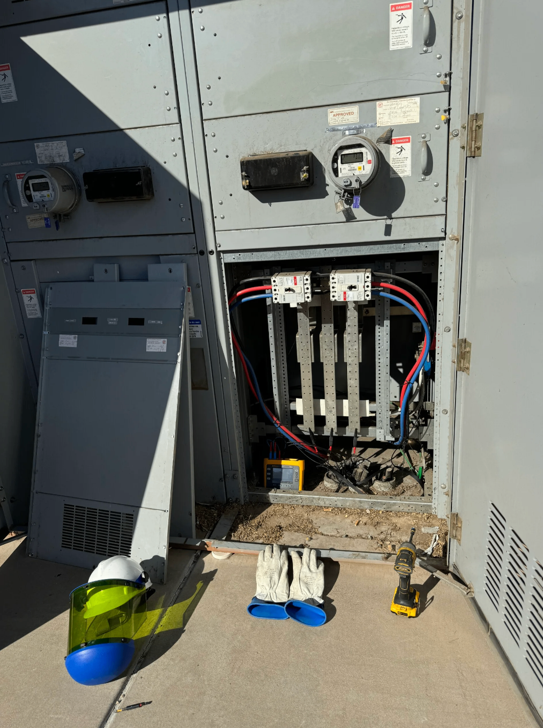 Open commercial electrical equipment with safety gear and tools staged in front